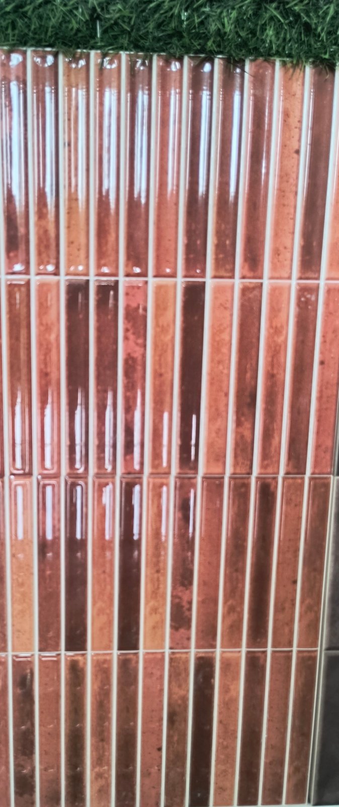 Tall glossy red-brown strip tiles in an icicle-style vertical pattern at Shri Tiles